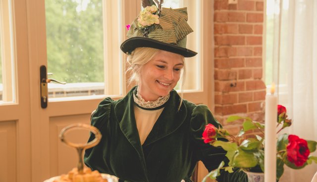 Pils dāma sēž pie galda 19.gs. tērpā